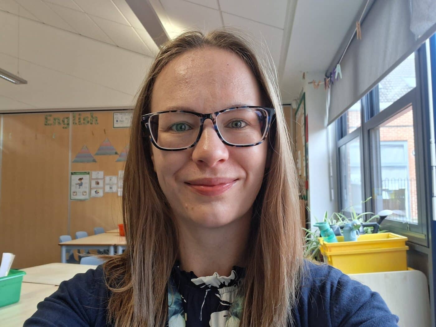 Danielle, Education Consultant at The SAW Trust, smiles in a bright classroom environment with educational displays and plants visible behind her.