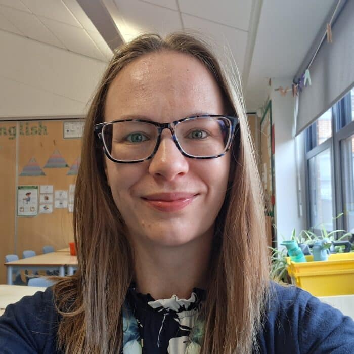 Danielle, Education Consultant at The SAW Trust, smiles in a bright classroom environment with educational displays and plants visible behind her.